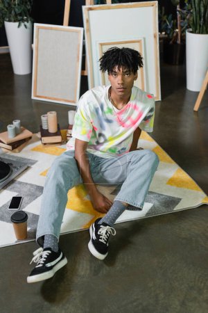 African american artist sitting near coffee and smartphone in art studio 