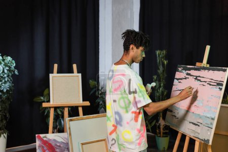 Téléchargez les photos : Vue latérale de la peinture d'artiste afro-américaine sur toile près de dessins en atelier - en image libre de droit
