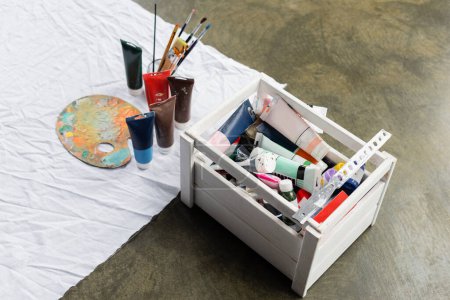 High angle view of paints in box near paints and palette on cloth 