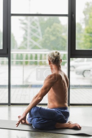 man in blue pants sitting in twisting yoga pose on mat in studio 