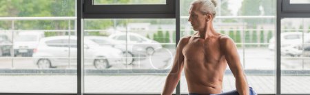 shirtless and grey haired man looking away in yoga studio, banner 