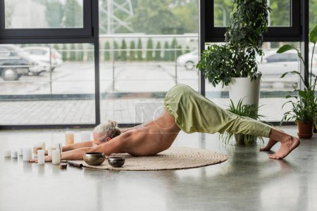 Photo for Side view of shirtless man stretching back while sitting in thunderbolt yoga pose near Tibetan singing bowls - Royalty Free Image