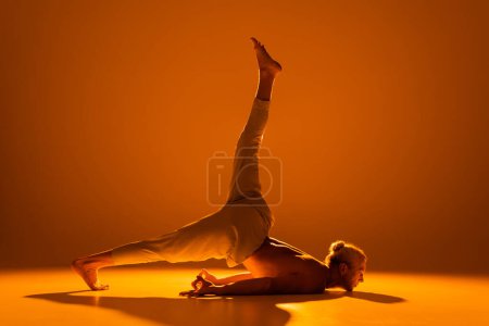 full length of shirtless man doing chin stand yoga pose on brown 