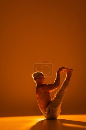 Foto de Full length of shirtless man doing boat yoga pose on brown - Imagen libre de derechos