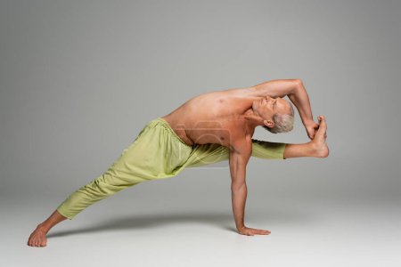 barefoot man in pants doing compass yoga pose on grey background 