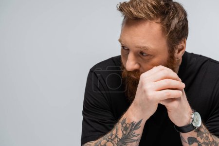 Foto de Tattooed pensive man holding hands near face and looking away isolated on grey - Imagen libre de derechos
