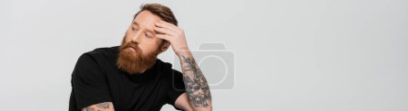 pensive bearded man in black t-shirt touching forehead and looking away isolated on grey, banner
