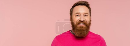 cheerful bearded man in magenta t-shirt smiling at camera isolated on pink, banner