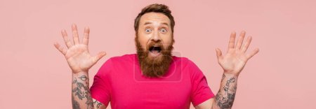 astonished bearded man with open mouth showing wow gesture isolated on pink, banner