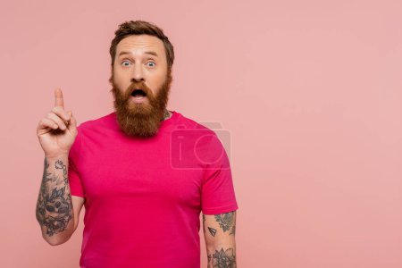 erstaunt tätowierter Mann zeigt Ideengeste, während er mit offenem Mund isoliert auf rosa steht