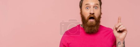 homme barbu étonné en t-shirt magenta lumineux montrant signe d'idée isolé sur rose, bannière