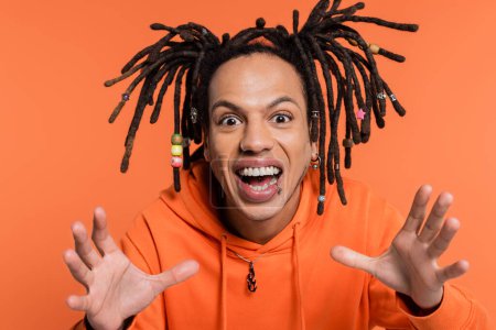 excited multiracial man with dreadlocks gesturing on coral background