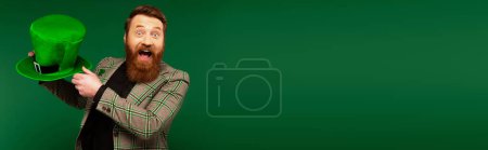 Téléchargez les photos : Excited man in jacket holding hat during saint patrick day isolated on green, banner - en image libre de droit