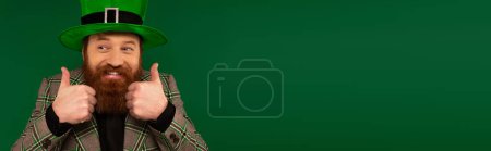 Photo for Bearded man in jacket and hat showing like gesture isolated on green, banner - Royalty Free Image