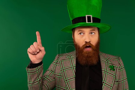 Thoughtful bearded man in hat with clover having idea isolated on green 