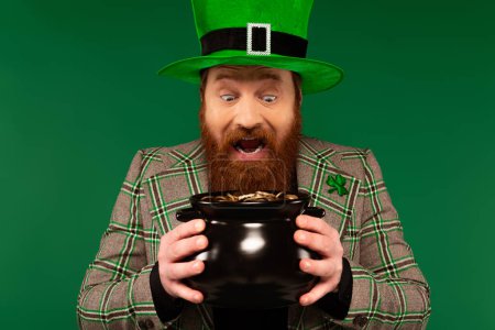 Téléchargez les photos : Amazed man in hat holding pot with golden coins isolated on green - en image libre de droit