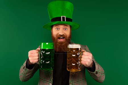 Photo for Positive man in hat holding glasses of beer during saint patrick day celebration isolated on green - Royalty Free Image