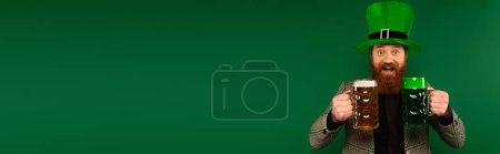 Foto de Bearded man holding beer while celebrating saint patrick day isolated on green with copy space, banner - Imagen libre de derechos