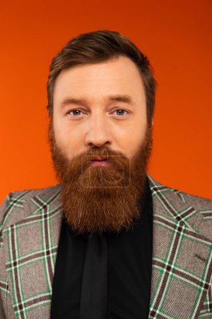 Portrait of bearded man in checkered jacket looking at camera isolated on red 