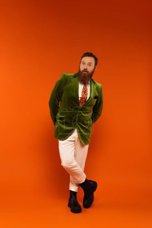 Full length of stylish man in velour jacket posing on red background 
