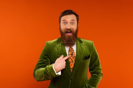 Excited bearded model in jacket pointing with finger at himself on red background 