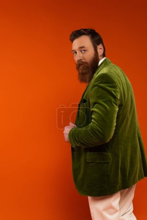 Stylish man in green velvet jacket looking at camera on red background 