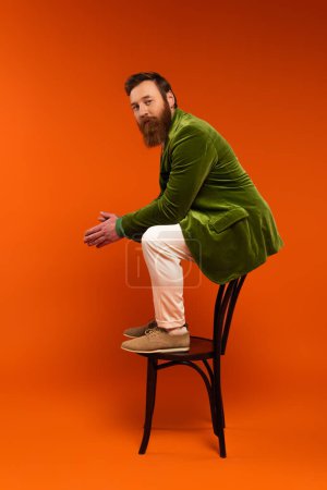 Trendy bearded model posing on chair on red background 