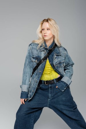 Photo for Young blonde woman in stylish denim clothes posing and looking away isolated on grey - Royalty Free Image
