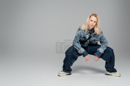 Foto de Full length of young blonde woman in stylish denim clothes posing on grey - Imagen libre de derechos