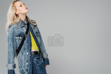 Téléchargez les photos : Femme blonde en jean élégant veste regardant loin isolé sur gris - en image libre de droit