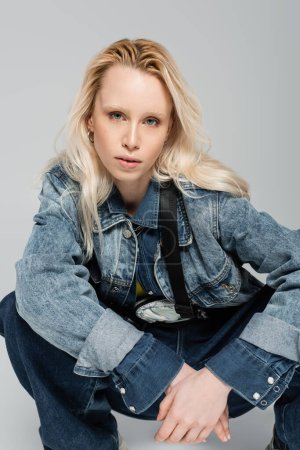 Photo for Blonde albino woman in stylish denim jacket with belt bag posing isolated on grey - Royalty Free Image