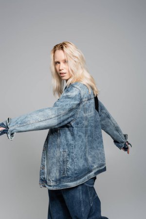 Foto de Young blonde woman in denim blue jacket posing with outstretched hands isolated on grey - Imagen libre de derechos