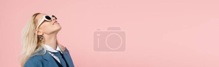 Téléchargez les photos : Femme blonde gaie en blazer bleu et lunettes de soleil souriant isolé sur rose, bannière - en image libre de droit