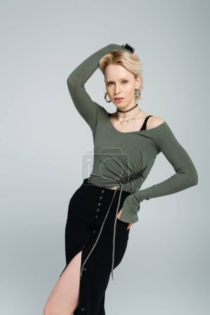 Blondine im langärmeligen Hemd und sexy Rock posiert mit der Hand an der Hüfte isoliert auf grau 