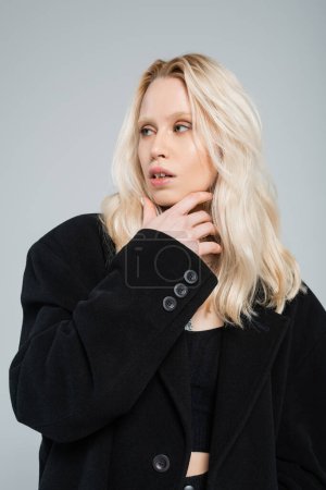 Photo for Blonde and young woman in stylish black coat posing isolated on grey - Royalty Free Image