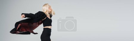 Foto de Young blonde woman in stylish black outfit jumping isolated on grey, banner - Imagen libre de derechos
