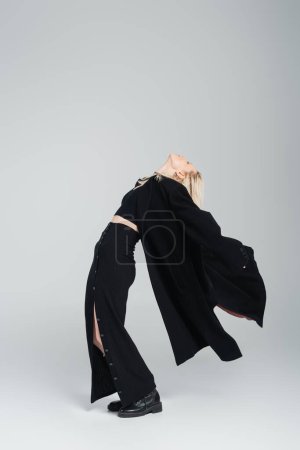 Foto de Longitud completa de la joven rubia en traje negro elegante posando con la cabeza levantada en gris - Imagen libre de derechos