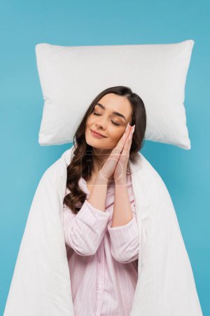 Photo for Young woman covered in white duvet sleeping on white flying pillow isolated on blue - Royalty Free Image