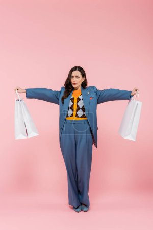 Müde Frau in blauem Hosenanzug, Einkaufstüten in der Hand und tief durchatmend auf rosa 