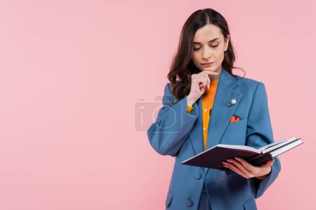 Photo for Pensive and brunette manager in blue blazer holding notebooks isolated on pink - Royalty Free Image