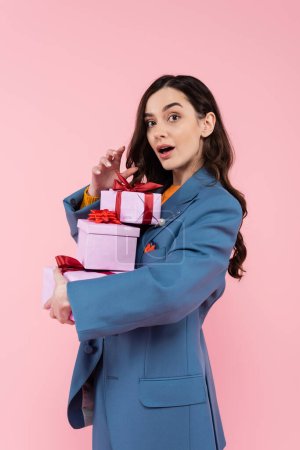 surprised woman with open mouth holding gift boxes with red ribbons isolated on pink