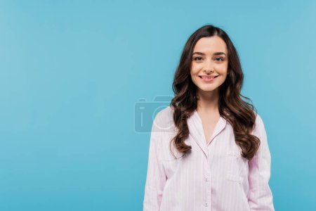 glückliche Frau im weißen Pyjama-Hemd lächelt vereinzelt in die Kamera auf blauem Grund