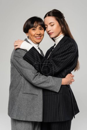 Foto de Joyful asian woman embracing young and stylish daughter standing with closed eyes isolated on grey - Imagen libre de derechos