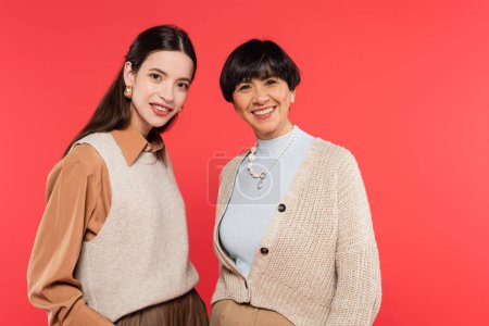 happy asian mother and daughter in stylish casual clothes smiling at camera isolated on coral