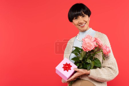 happy asian woman holding roses and presents isolated on coral background 