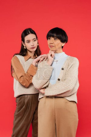 young asian woman leaning on shoulder of brunette mother isolated on coral 