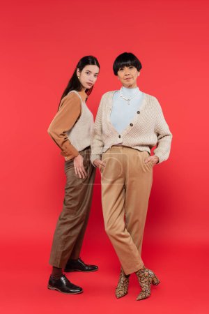 full length of asian mother and daughter in trendy clothes posing on coral background 