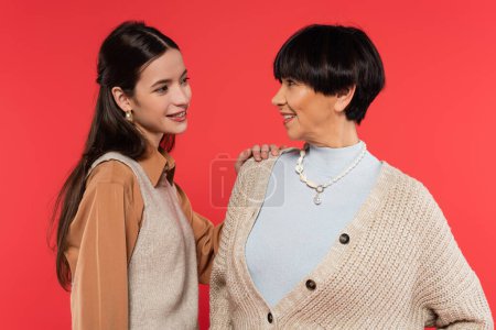 smiling asian mother and daughter looking at each other isolated on coral 