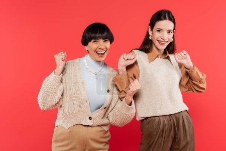 excited asian mother and daughter in stylish clothes celebrating isolated on coral 