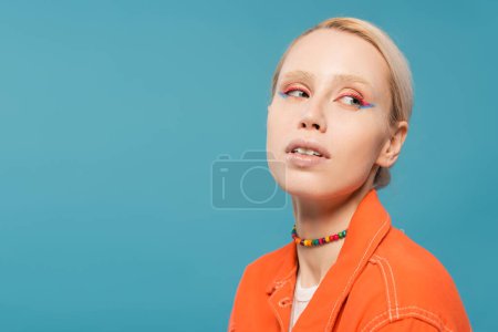 Téléchargez les photos : Portrait de jolie femme blonde en perles colorées et veste orange vif regardant loin isolé sur bleu - en image libre de droit